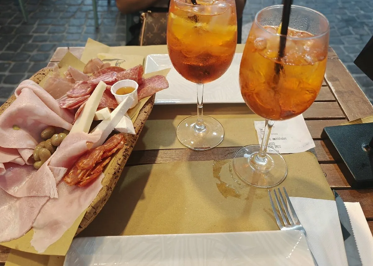Tagliere di salumi e formaggi con due spritz su un tavolo esterno, sul selciato del Corso
