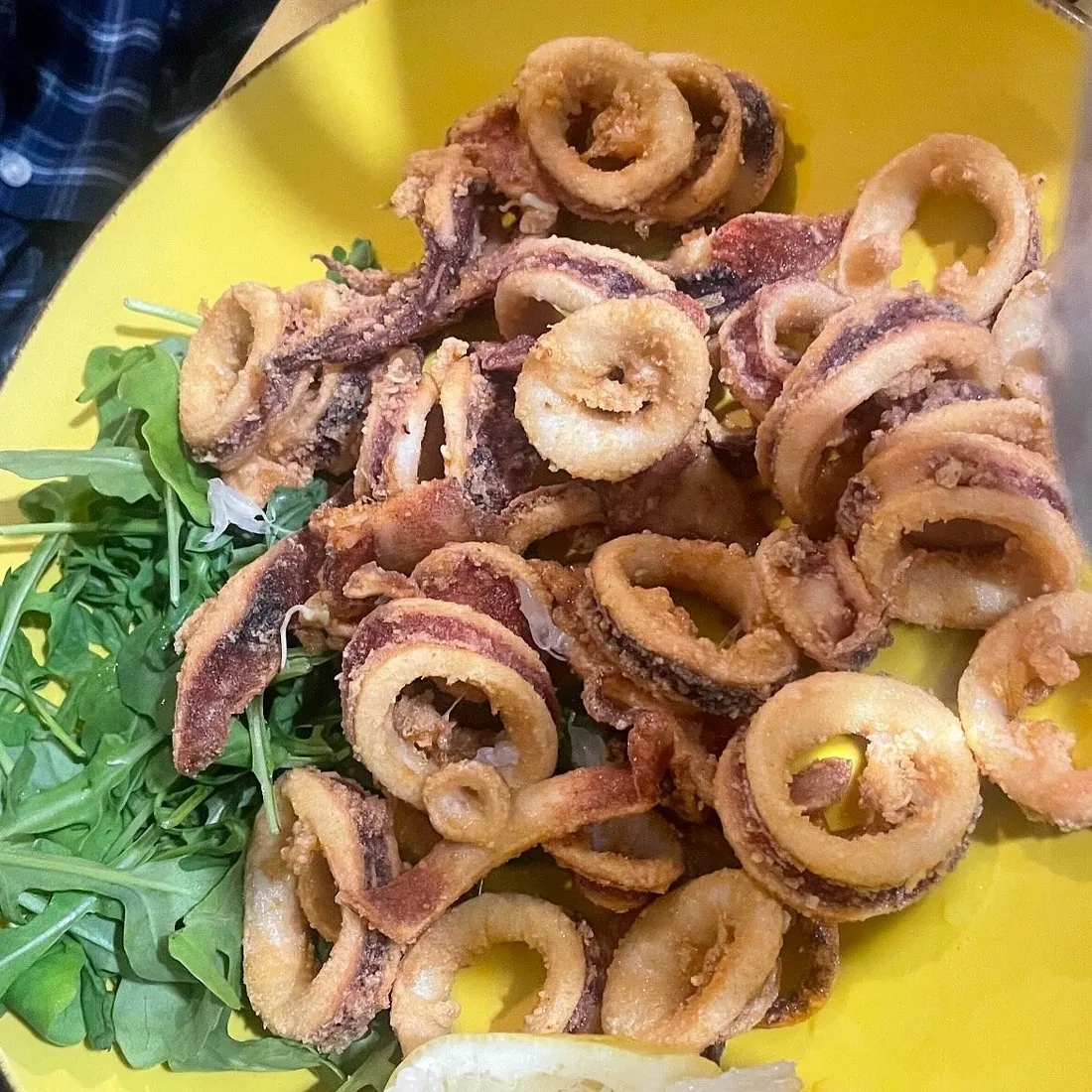 Piatto giallo di anelli e ciuffi di calamari fritti su un letto di rucola