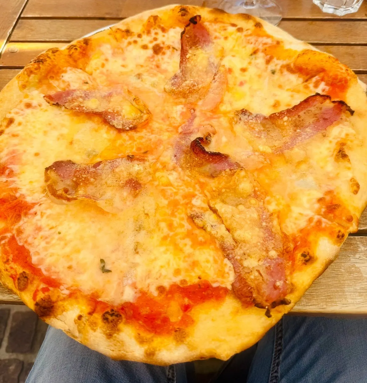 Pinsa rossa con mozzarella e strisce di guanciale croccante, vista dall'alto su un tavolo di legno