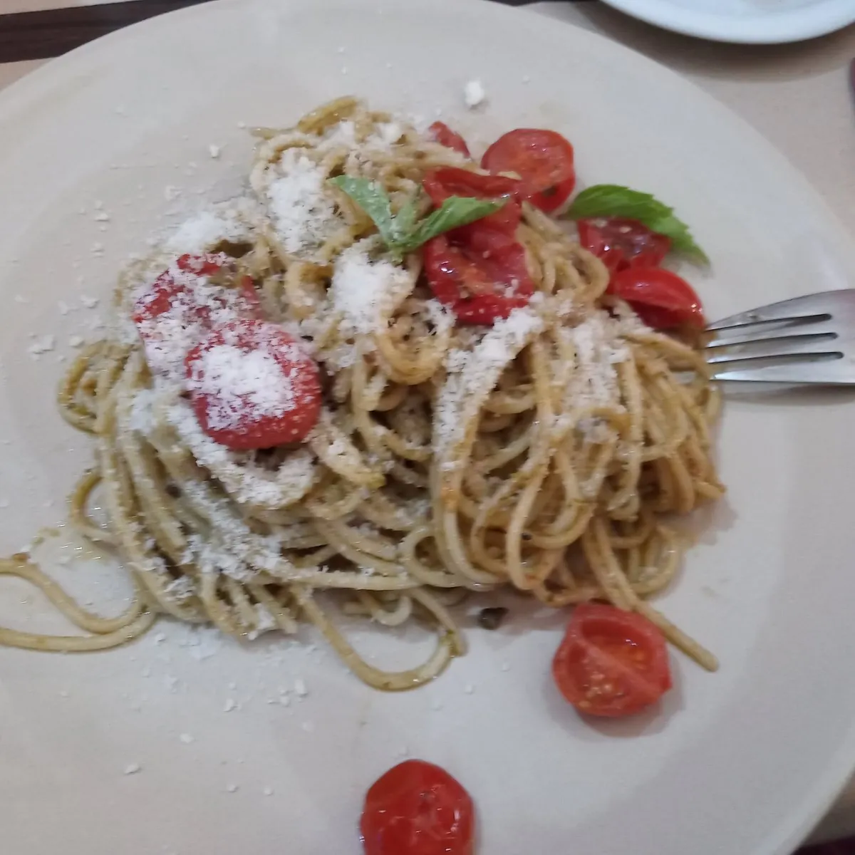 Piatto di spaghetti al pesto con pomodorini e grana grattugiato