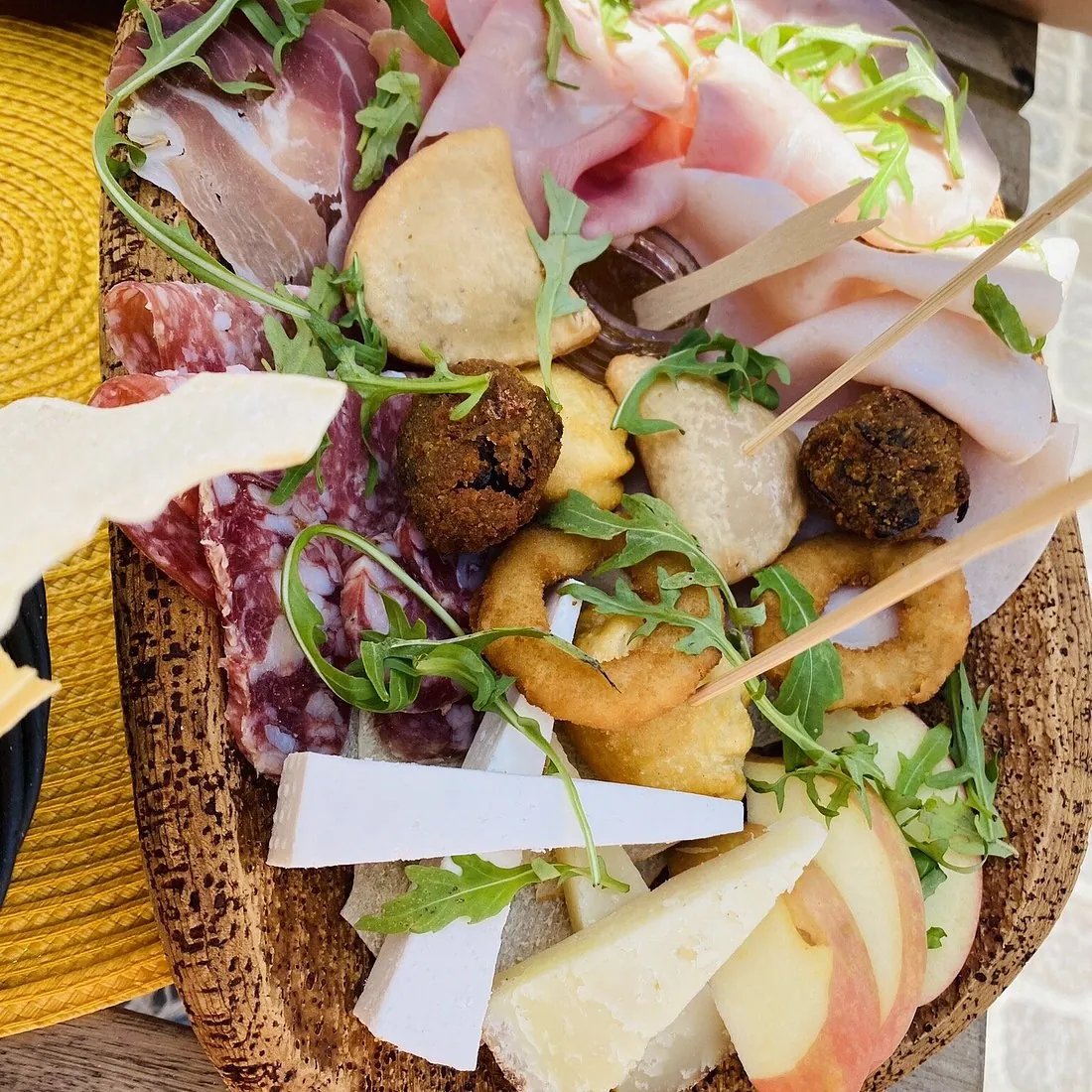 Tagliere di legno con salumi, formaggi sardi, olive, polpettine fritte e pane carasau, servito al tavolo